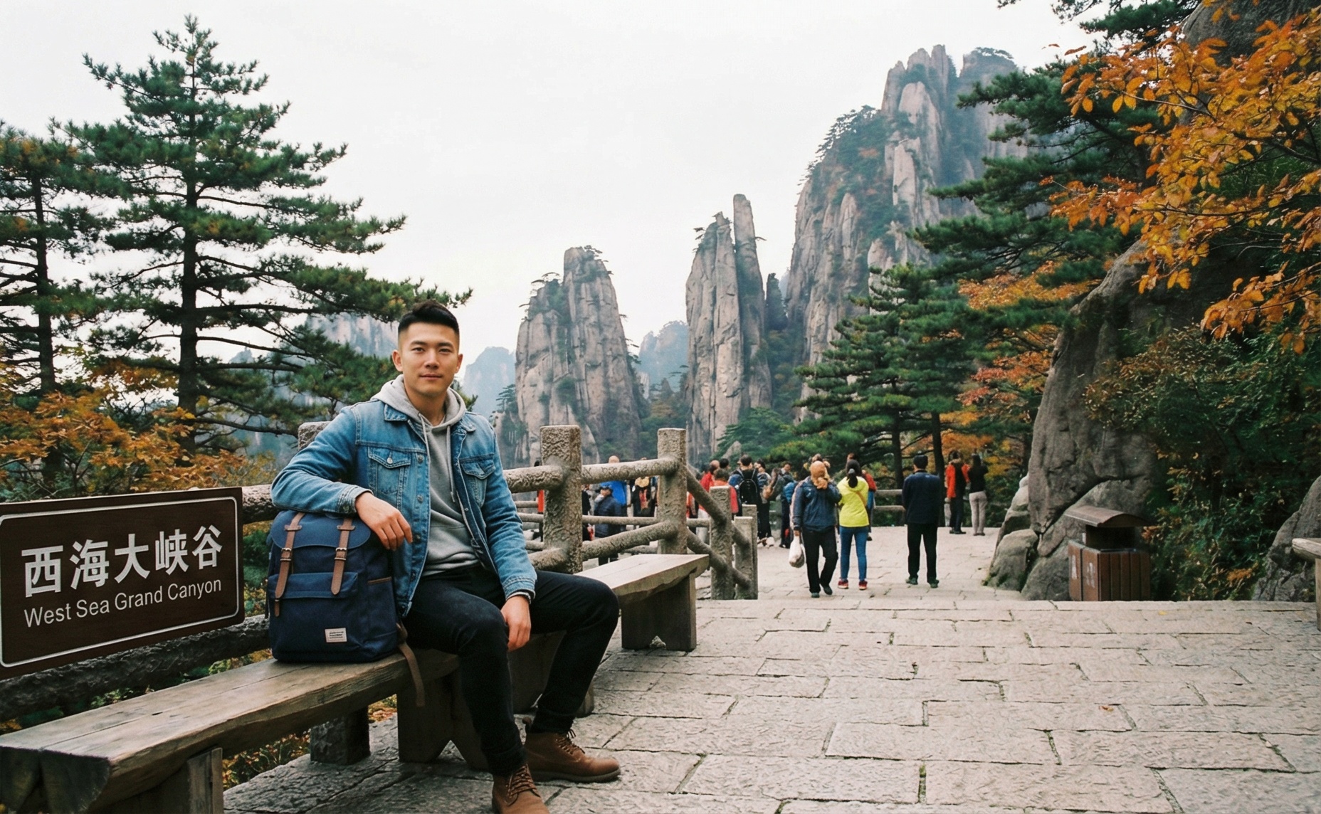 Photo-realistic edit of the reference photo. Keep the original West Sea Grand Canyon background, stone path, railings, autumn trees and tourists in the distance. Replace the elderly man on the bench with a handsome young male celebrity-looking man in his late 20s, stylish haircut, clear skin, natural smile, casual but fashionable outdoor outfit (light jacket, shirt, jeans, sneakers), holding a backpack beside him in a relaxed pose. Maintain the same camera angle and composition, soft daylight, realistic colors, high resolution travel photography style.